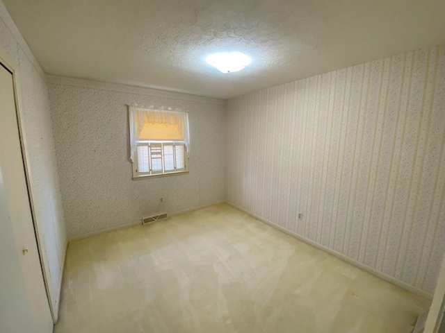 carpeted spare room featuring wallpapered walls, visible vents, and a textured ceiling