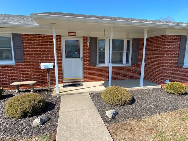 property entrance featuring brick siding, a porch, and roof with shingles