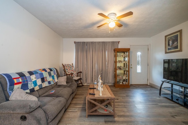 living area with ceiling fan, a textured ceiling, baseboards, and wood finished floors