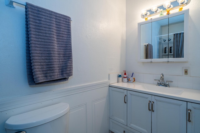 bathroom with a shower with shower curtain, a wainscoted wall, vanity, and toilet