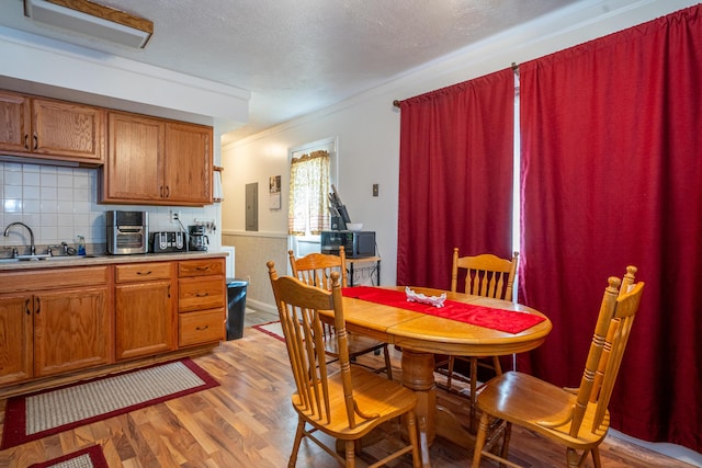 dining area with light wood-style floors, wainscoting, crown molding, and a textured ceiling