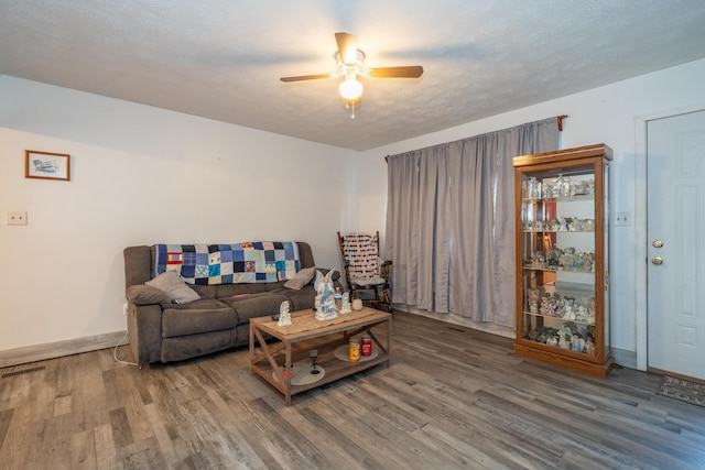 living room with ceiling fan, a textured ceiling, baseboards, and wood finished floors