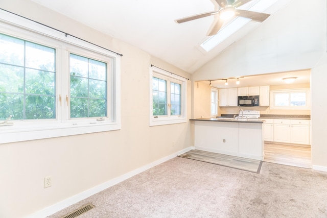 kitchen featuring black microwave, light carpet, healthy amount of natural light, baseboards, and lofted ceiling