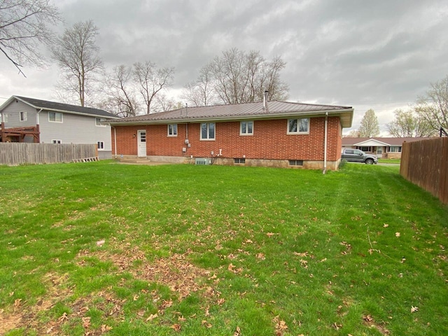 rear view of house featuring fence, brick siding, a yard, and metal roof