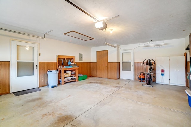 garage featuring a garage door opener, electric panel, a wainscoted wall, and wood walls