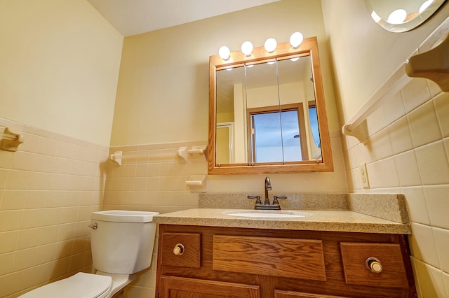 bathroom featuring wainscoting, tile walls, toilet, and vanity