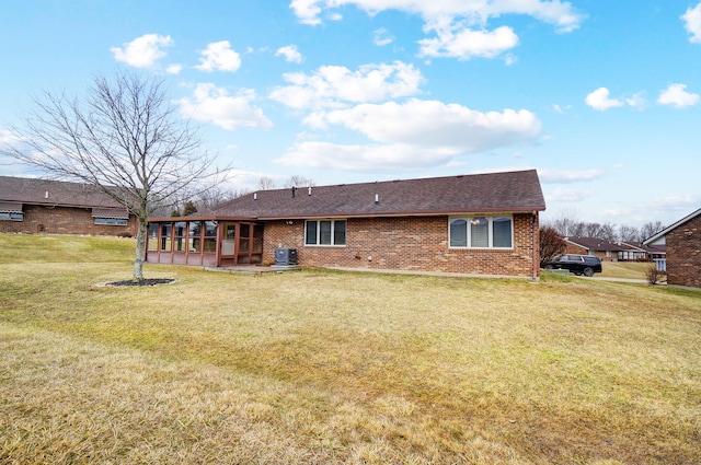 rear view of property featuring brick siding, a lawn, a shingled roof, and a sunroom