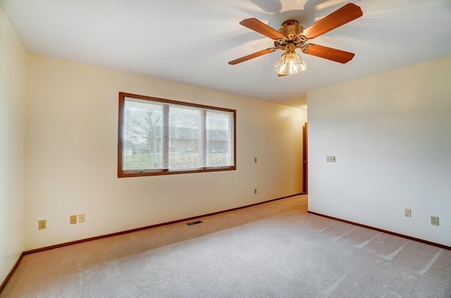 spare room with light colored carpet, visible vents, ceiling fan, and baseboards