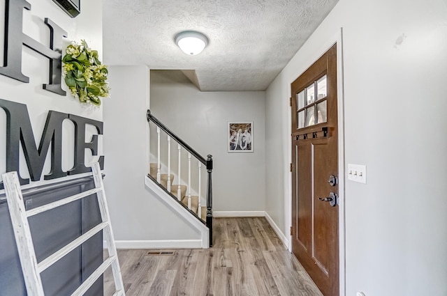 foyer with a textured ceiling, wood finished floors, visible vents, baseboards, and stairway