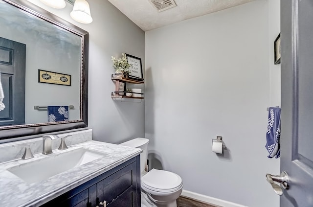 bathroom featuring visible vents, toilet, vanity, wood finished floors, and baseboards