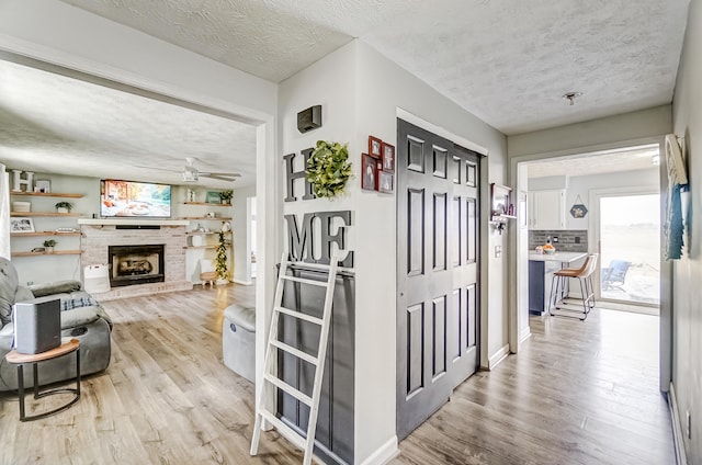 hallway with light wood-style floors, a textured ceiling, and baseboards