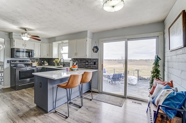 kitchen featuring light wood-style flooring, a peninsula, a sink, light countertops, and appliances with stainless steel finishes