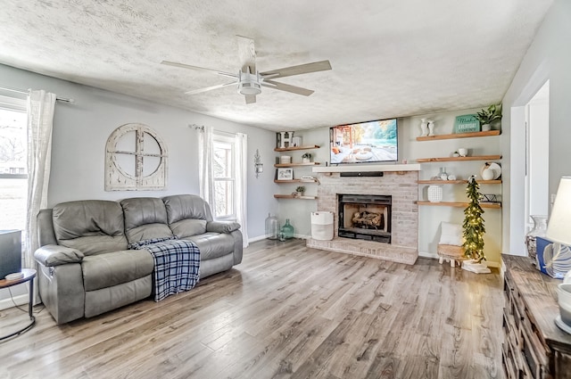 living room featuring a fireplace, a ceiling fan, a textured ceiling, and wood finished floors