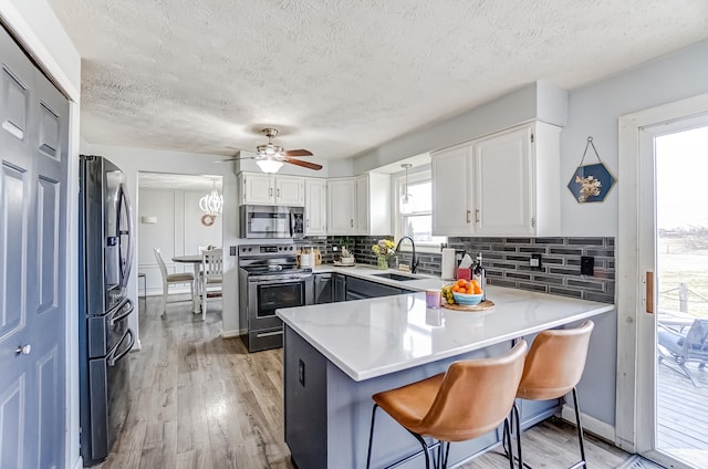 kitchen featuring decorative backsplash, light wood-style flooring, a peninsula, stainless steel appliances, and a sink