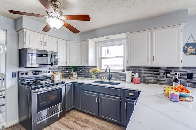 kitchen featuring backsplash, light wood-style flooring, appliances with stainless steel finishes, white cabinets, and a sink