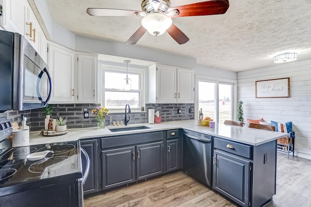 kitchen with a peninsula, range with electric cooktop, a sink, white cabinetry, and stainless steel dishwasher