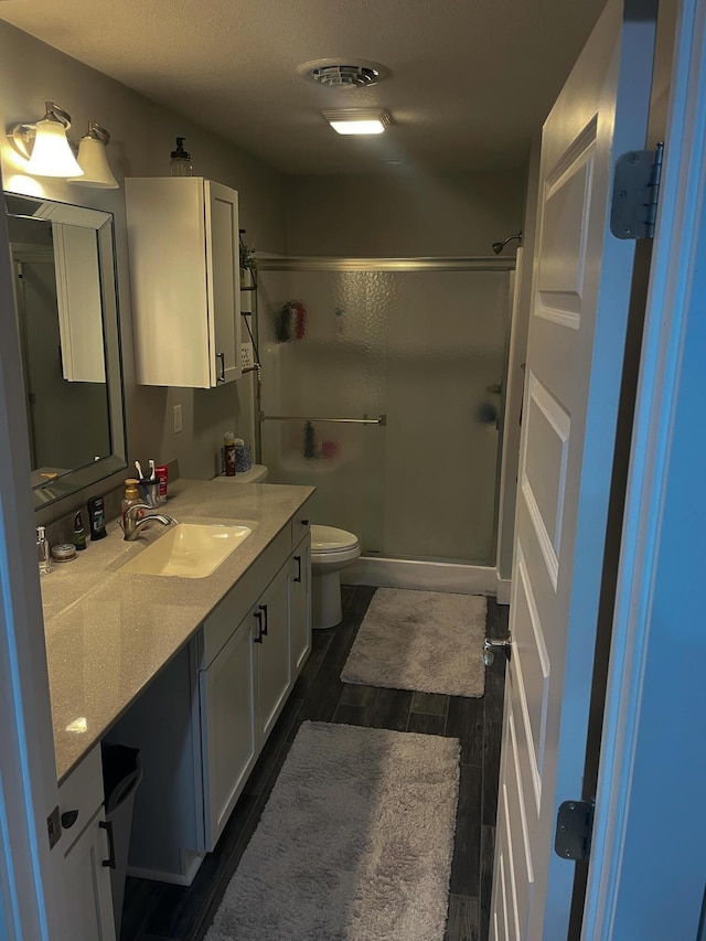 bathroom with a stall shower, visible vents, toilet, vanity, and wood finish floors