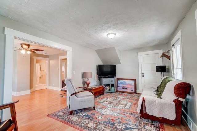 living room featuring ceiling fan, a textured ceiling, and light wood-type flooring