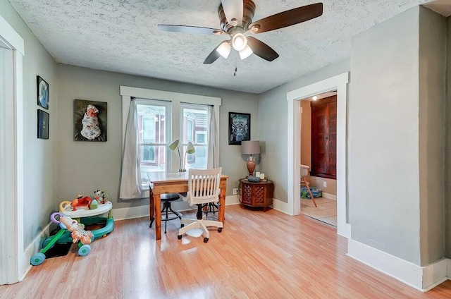 home office with ceiling fan, light hardwood / wood-style floors, and a textured ceiling