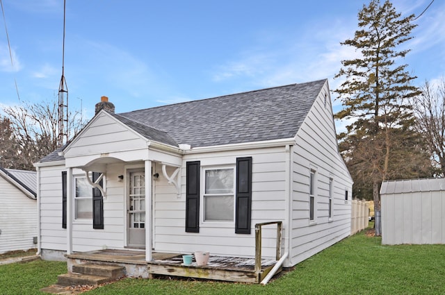 bungalow with a shingled roof, a chimney, and a front lawn