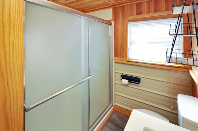 bathroom with toilet, a stall shower, and wooden walls