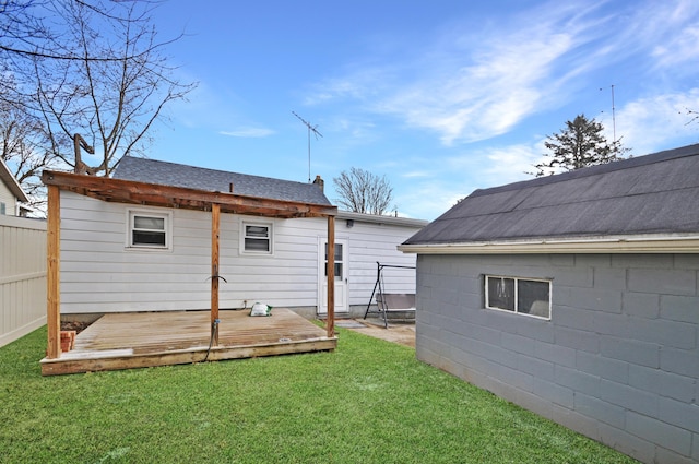 rear view of house featuring fence, a deck, a lawn, and roof with shingles