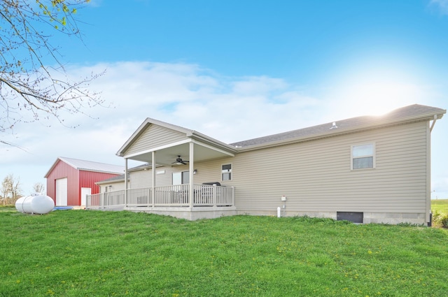 back of property with an outdoor structure, a lawn, and a ceiling fan