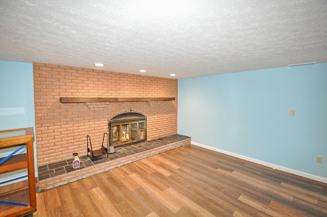 unfurnished living room with a brick fireplace, a textured ceiling, wood finished floors, and baseboards