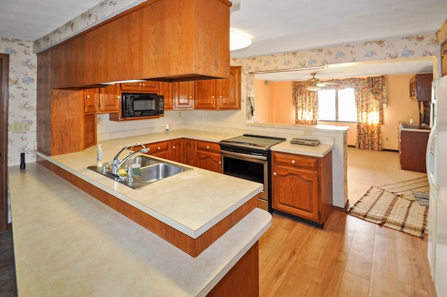 kitchen with stainless steel electric range oven, a sink, black microwave, wallpapered walls, and a peninsula