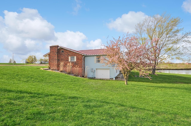 back of house featuring a chimney, an attached garage, metal roof, a water view, and a lawn