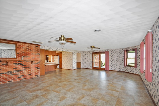 unfurnished living room with wallpapered walls and ceiling fan