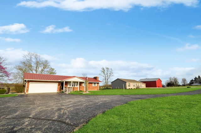 single story home featuring aphalt driveway, a chimney, metal roof, a front yard, and a garage