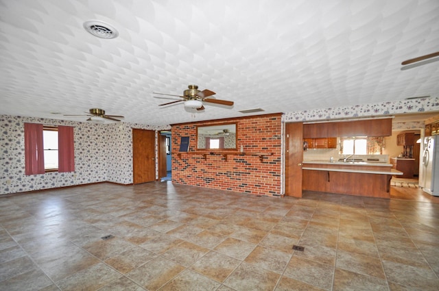 unfurnished living room featuring a ceiling fan, visible vents, and wallpapered walls