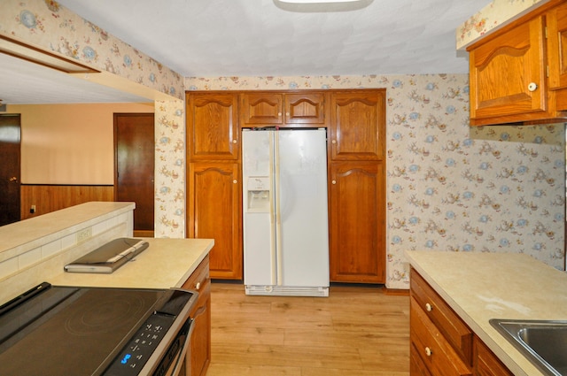 kitchen with light wood-type flooring, white refrigerator with ice dispenser, light countertops, wallpapered walls, and electric range