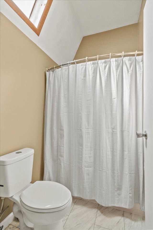 bathroom with vaulted ceiling with skylight, toilet, marble finish floor, and a shower with curtain