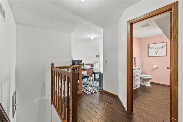 corridor featuring dark wood-type flooring, visible vents, baseboards, and a textured ceiling