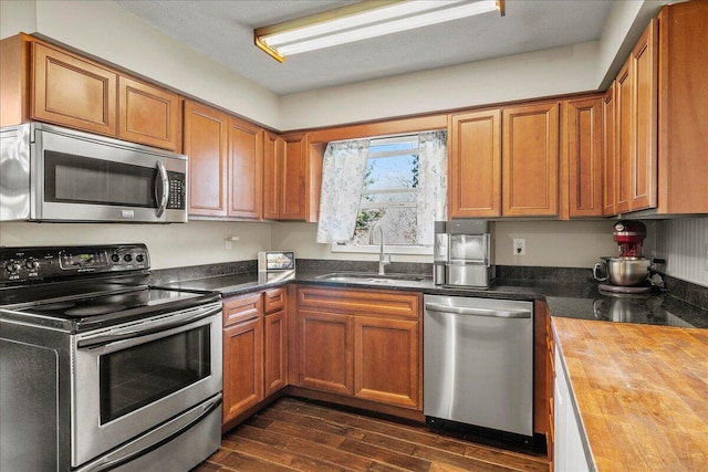 kitchen with brown cabinetry, a sink, stainless steel appliances, dark wood-type flooring, and wood counters