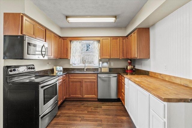 kitchen with dark wood-type flooring, appliances with stainless steel finishes, brown cabinetry, a textured ceiling, and a sink