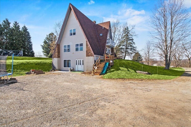 rear view of house featuring a lawn, a trampoline, stairs, a shingled roof, and a chimney