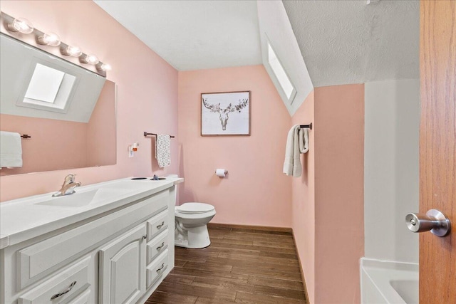 full bath featuring vaulted ceiling with skylight, toilet, vanity, and wood finished floors