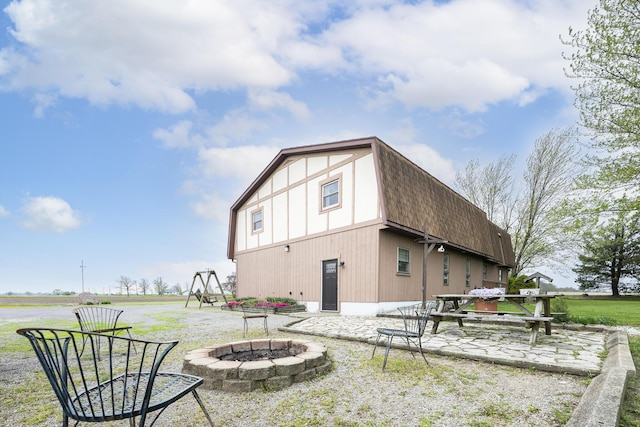 back of house featuring a shingled roof, an outdoor fire pit, a gambrel roof, and a patio area
