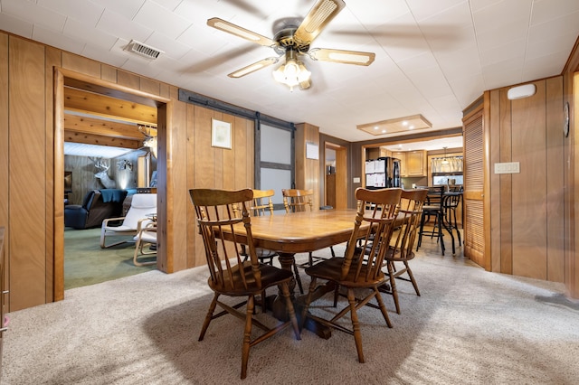dining room featuring visible vents, carpet flooring, wooden walls, and a barn door