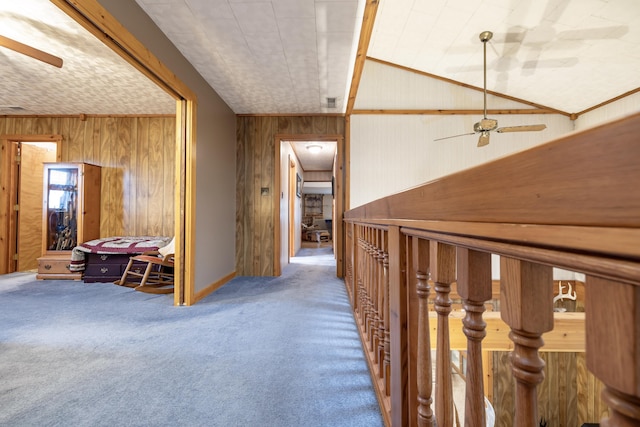hallway featuring carpet floors, wood walls, and vaulted ceiling