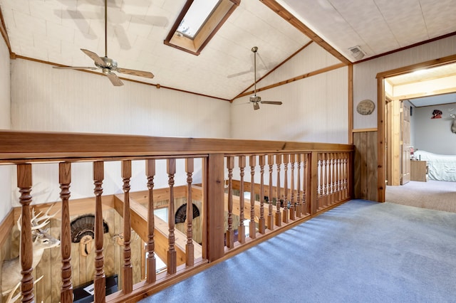 hallway featuring visible vents, wood walls, wainscoting, vaulted ceiling with skylight, and carpet flooring