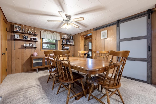 carpeted dining space featuring a ceiling fan, wood walls, and a barn door