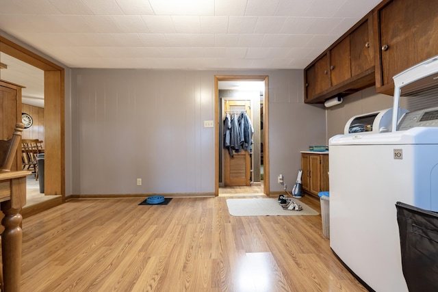 clothes washing area featuring washer / clothes dryer, baseboards, light wood finished floors, and cabinet space