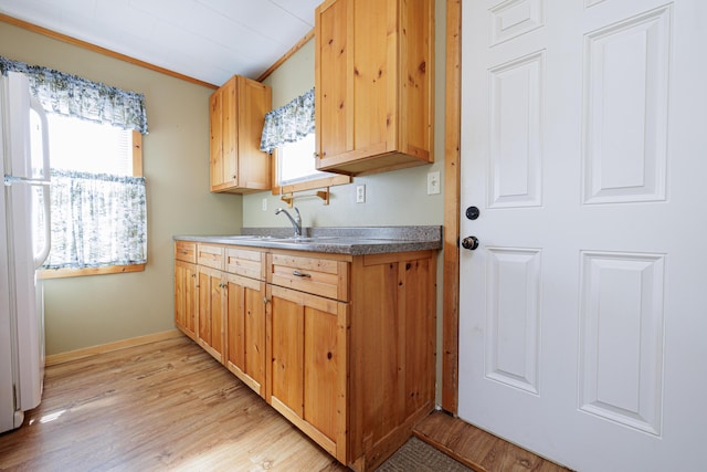 kitchen with a sink, light wood-style floors, ornamental molding, freestanding refrigerator, and dark countertops