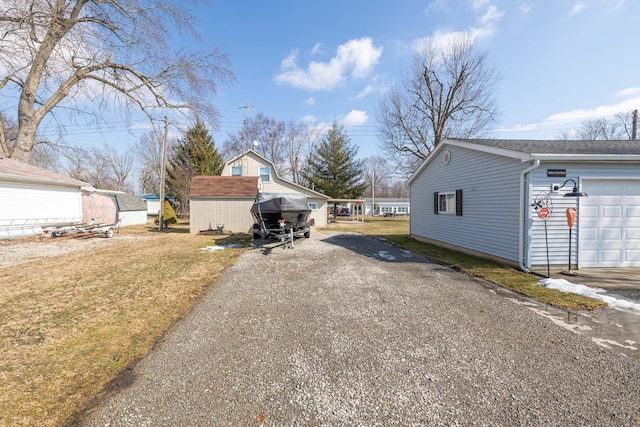 view of side of home with driveway, a storage shed, a garage, a lawn, and an outbuilding