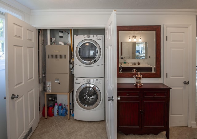 laundry area with laundry area, light tile patterned flooring, crown molding, and stacked washing maching and dryer