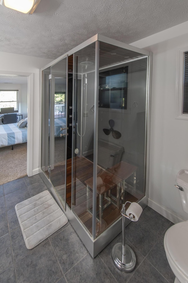 ensuite bathroom featuring toilet, ensuite bathroom, a stall shower, a textured ceiling, and baseboards